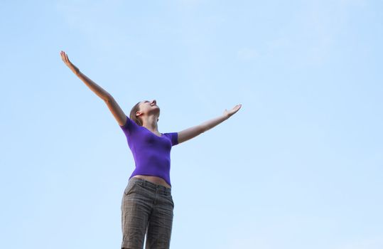 Young woman staying with raised hands against blue sky