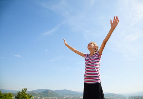 Teenage girl staying with raised hands against blue sky