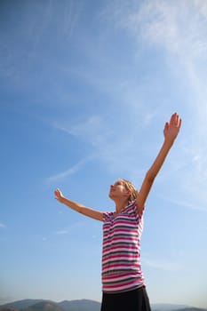 Teenage girl staying with raised hands against blue sky