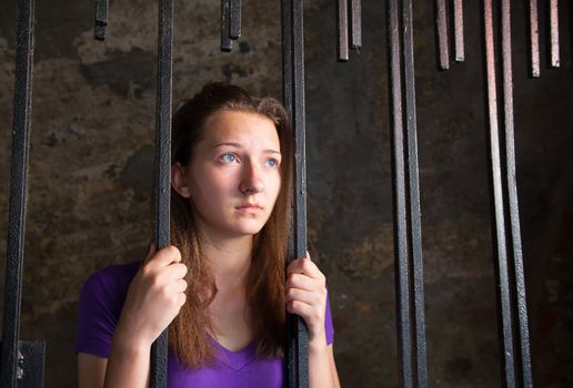 Young woman looking from behind the bars