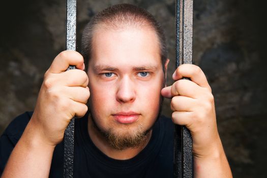 Young man looking from behind the bars