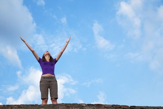 Young woman staying with raised hands against blue sky