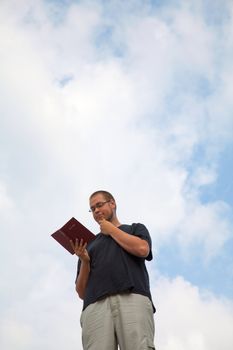 Young man staying with the Bible against blue sky