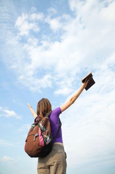 Teenage girl staying with raised hands against blue sky