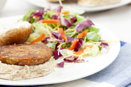 Veggie burger pattie on a bun with a fresh green salad.
