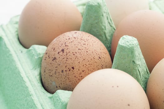Brown eggs in green packaging, one speckled.