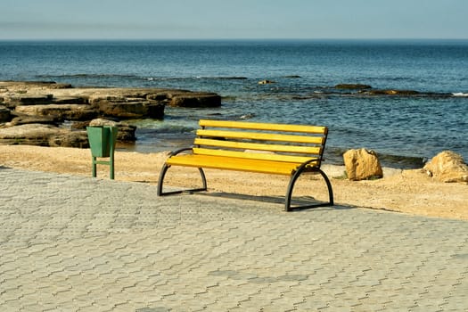 Empty wooden bench on a paved promenade overlooking a rocky coastline at the seaside