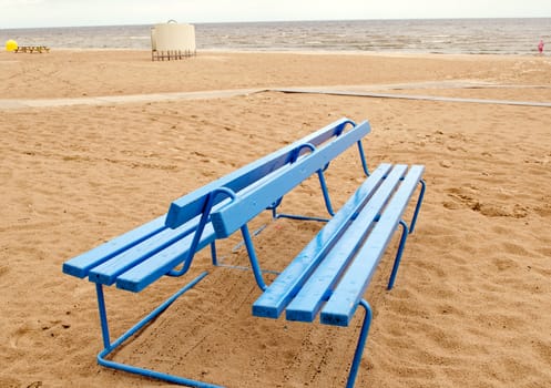 Blue bench on seaside sand after rain. Bathing box in beach.