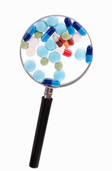 Group of different pills on magnifying glass. On white background.