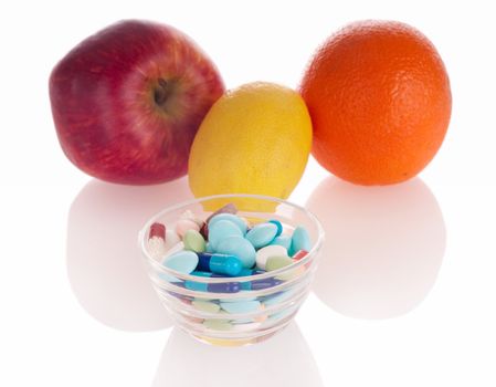 Concept of vitamin medicine with different pills in glass bowl and defocused fruits on background with soft shadows
