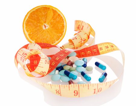 Concept of diet and medicine.  Heap of pills, orange slice and measuring tape with reflection on white background. Focus on pills