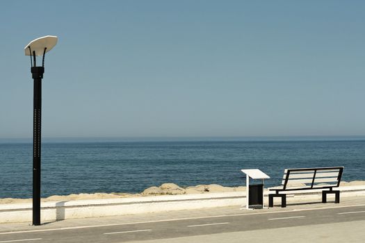 Empty bench and lamppost alongside a road on a promenade overlooking the ocean on a sunny summer day