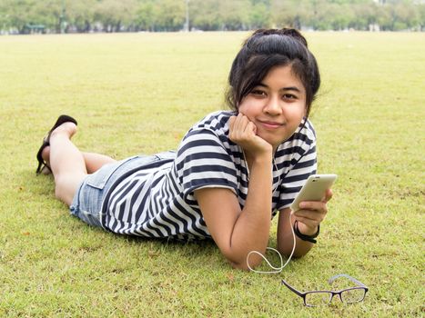 A young girl lie down on grass with headphones outdoors. Listening music 