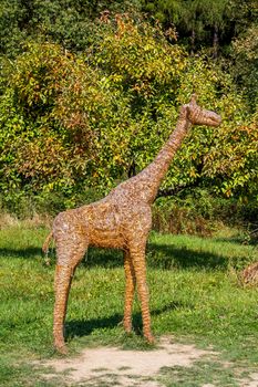 abstract straw giraffe in zoo park with green trees in background