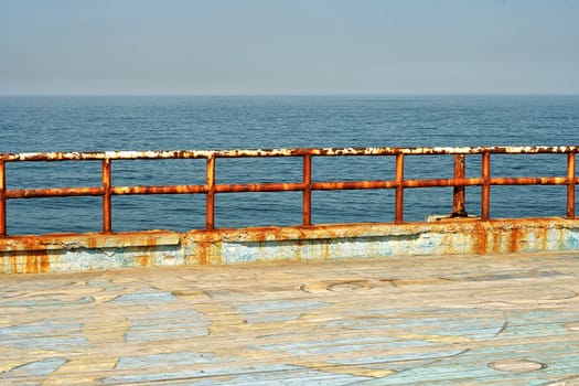 Grungy metal railings covered in red rust and corrosion caused by the salt water at the seaside