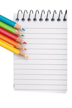 A vivid image with various colored pencils such as yellow, orange, red and blue on a notebook.
