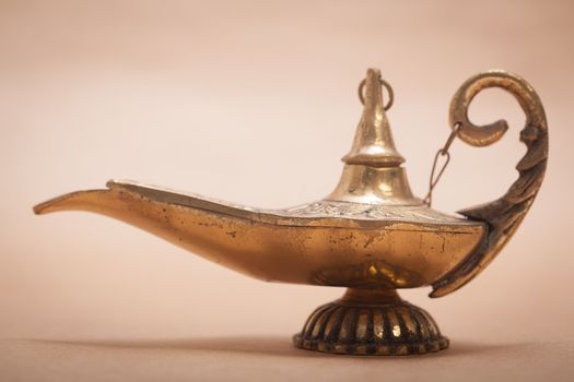 A magic genie lamp, isolated on a sand color background, in a studio shot.