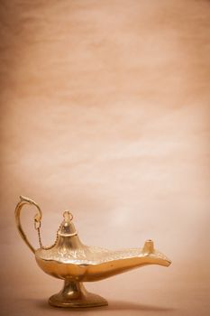 A magic genie lamp, isolated on a sand color background, in a studio shot.