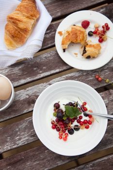 breakfast table with croissants, berries, yogurt and eggs