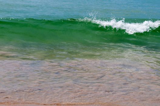 Small calm wave with clean turquoise water on sandy shallow beach. Focus in front.
