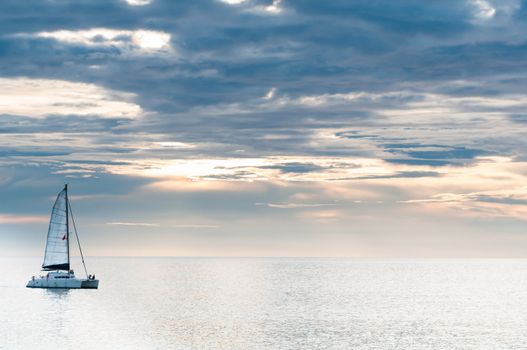 Sailing yacht in sunset on tranquil sea and cloudy sky