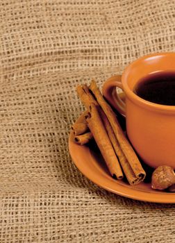 Closeup shot of freshly prepared cup of italian espresso with cinnamon, coffe beans, nuts and lemon over sacking