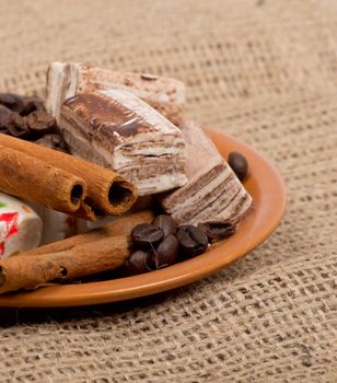 Sweets, cinnamon, nuts and coffee beans on a saucer, on burlap background.
