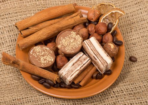 Sweets, cinnamon, nuts and coffee beans on a saucer, on burlap background.