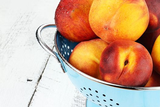 Blue colander filled with freshly washed peaches over a rustic background.
