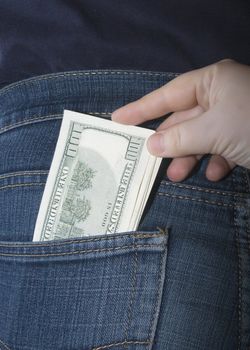 Bundle of dollars in a jeans rear pocket and a hand pulling them out