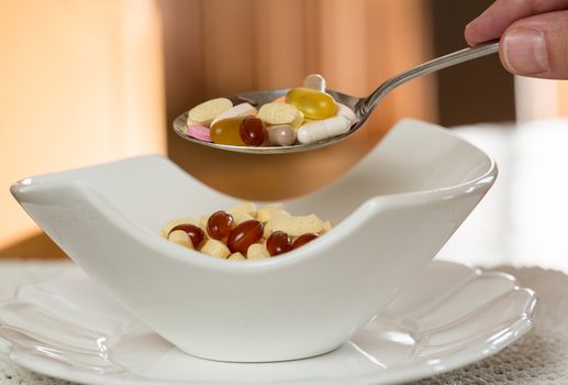 Spoonful of vitamin tablets suspended over bowl of tablets for breakfast in kitchen