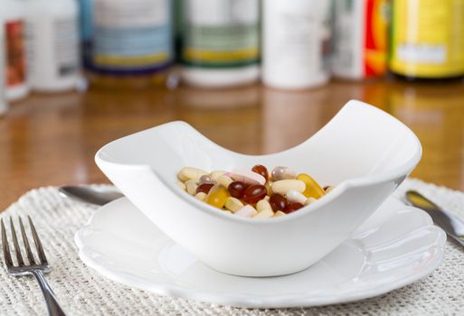 Vitamins in bowl of tablets for breakfast in kitchen with rows of bottles in background
