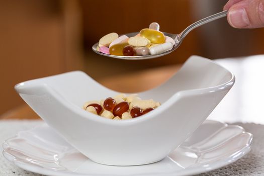 Spoonful of vitamin tablets suspended over bowl of tablets for breakfast in kitchen