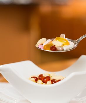 Spoonful of vitamin tablets suspended over bowl of tablets for breakfast in kitchen