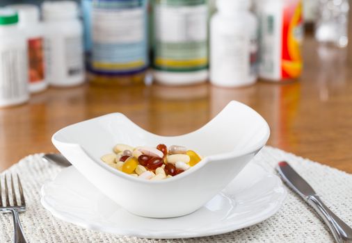 Vitamins in bowl of tablets for breakfast in kitchen with rows of bottles in background
