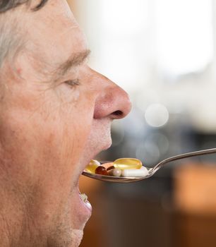 Senior caucasian male eating a spoonful of vitamin tablets for breakfast in kitchen