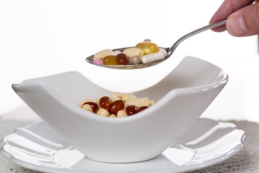 Spoonful of vitamin tablets suspended over bowl of tablets for breakfast in kitchen