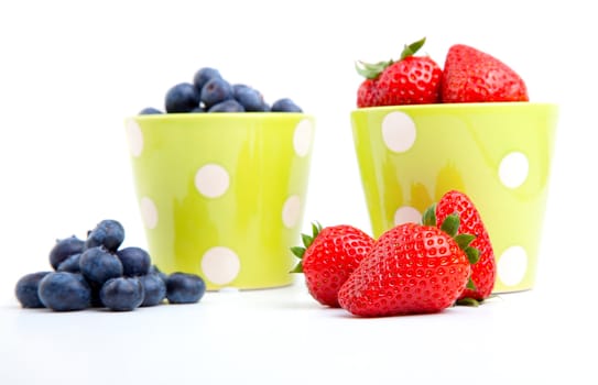 Assorted fresh picked berries in a green mug over a white background. Vertical format with reflection.