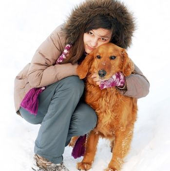 smiling teenager caucasian girl in hood hugging her dog outdoors at snow