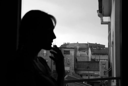 woman silhouette looking out window indoors, black and white