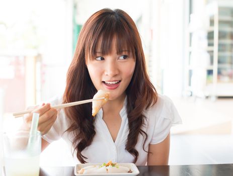 Eating rice noodle roll (chee cheong fun) at restaurant. Young Asian girl eating breakfast Cantonese cuisine dim sum using chopsticks.