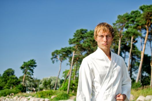 Young man in kimono on sky and trees background