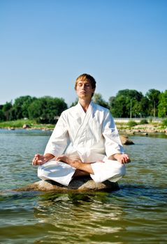 Man in kimono meditating on the rock in the sea