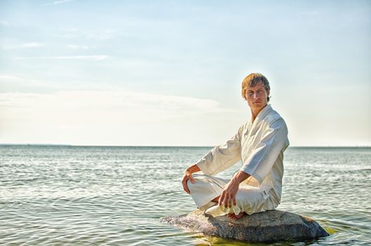 Man in kimono meditating on the rock in the sea