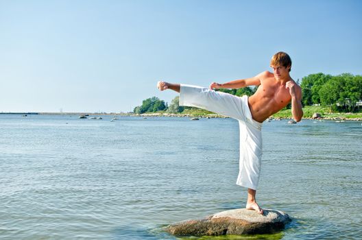 Man in kimono training on the rock in the sea