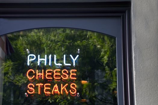 Neon sign for Philly Cheese Steaks in the door of a restaurant.