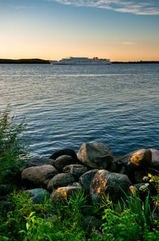 Landscape with rocky coastline and remote ship at sunset