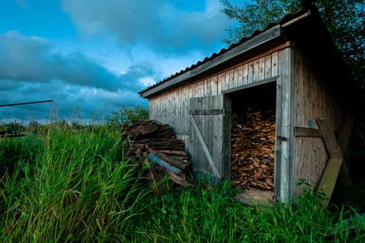 Old and hand made barn for firewood with grass and beautiful cloudscape