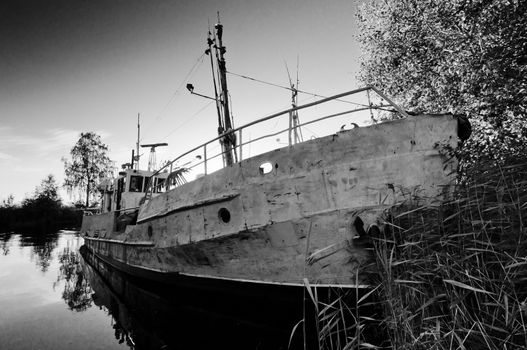 Old, rusty and damaged ship on still water in black and white