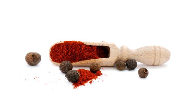 Wooden scoop in heap of pepper with peppercorns of sweet pepper on white background and focus on scoop.